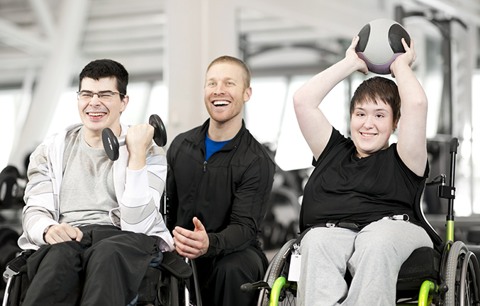 Young man and young woman in wheelchairs using gym equipment and working out with a trainer