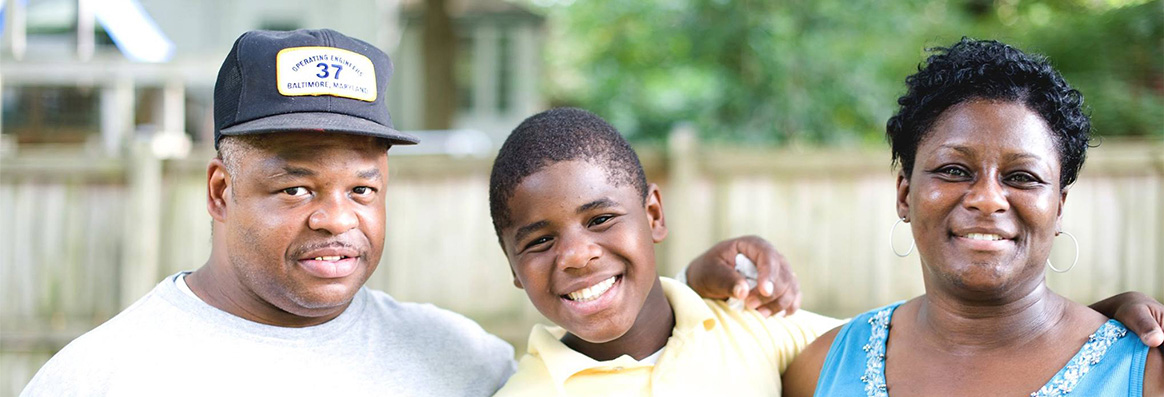 Portrait of African-American parents standing on either side of adolescent boy with trees and a fence in the background