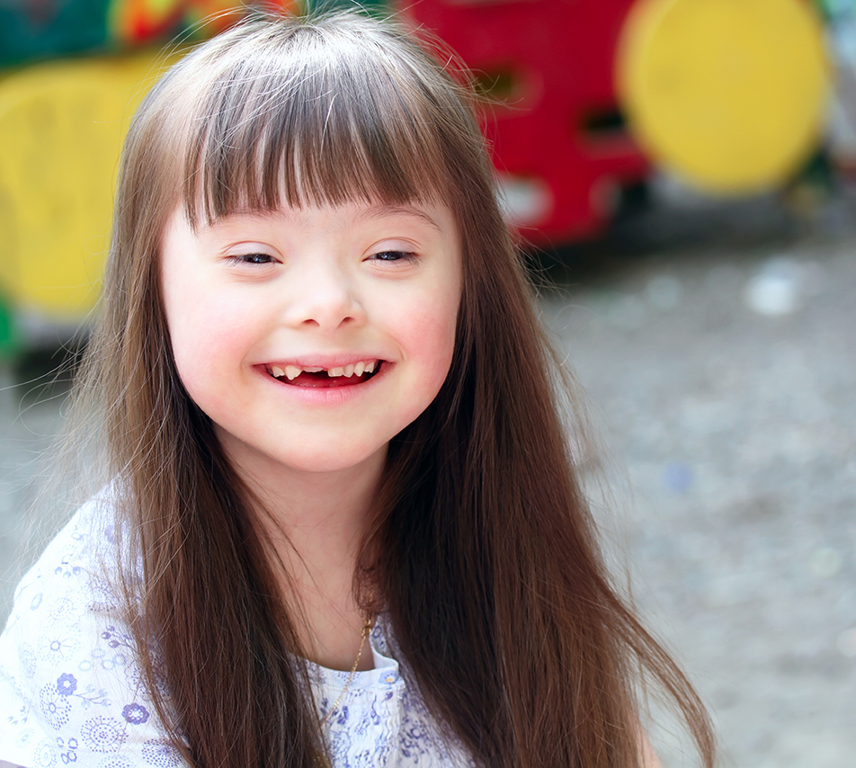3-Guiding-Principles Portrait of a smiling young girl with Down syndrome at a playground.