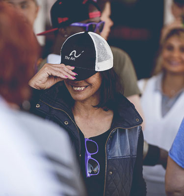 Smiling woman wearing a hat with The Arc's logo pulled down over her eyes