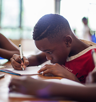 Elementary-school age boy sits at a desk and focuses intently on what he is writing