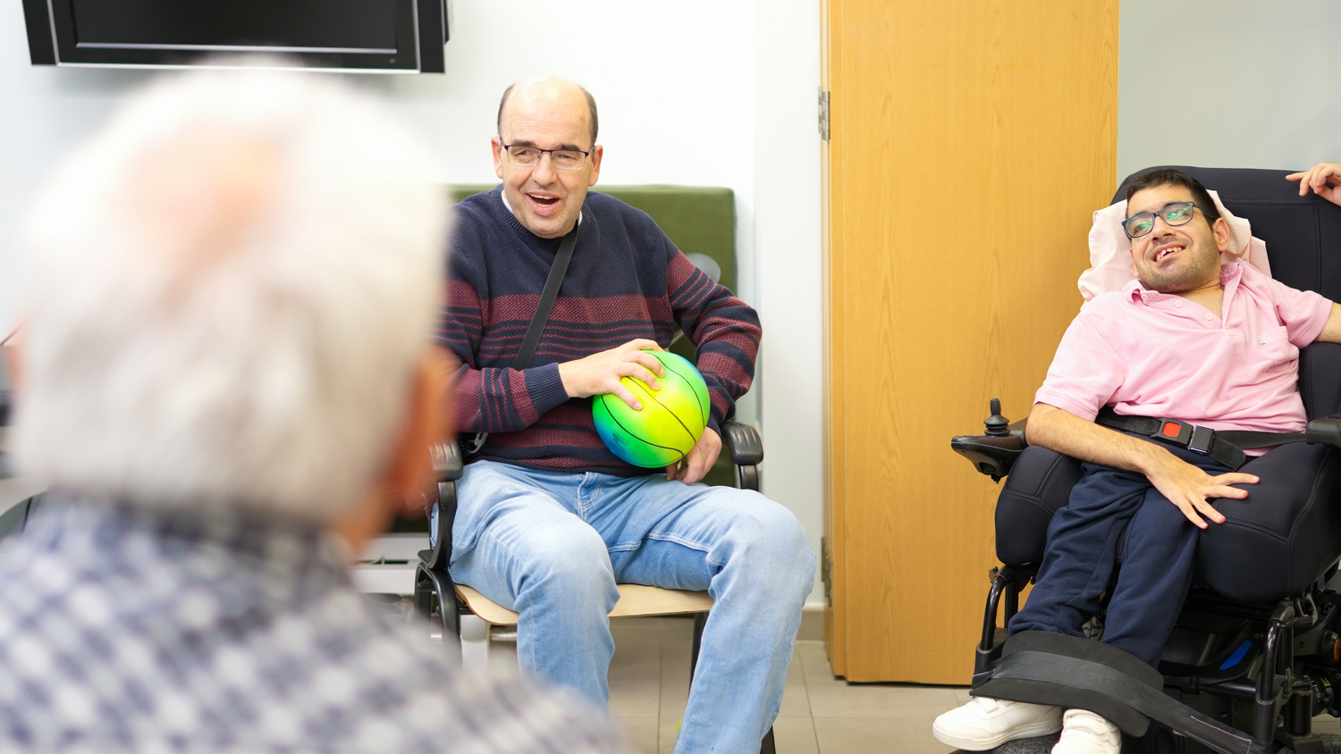 Several individuals with disabilities sitting in a room playing with a ball