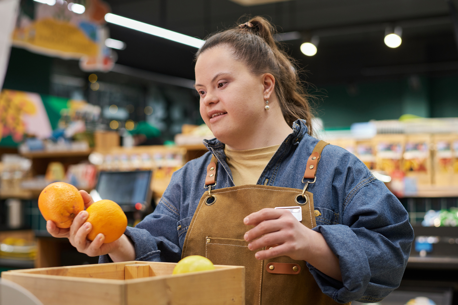 Woman with down syndrome working at a grocery store holding oranges